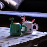 ماگ دایناسوری در دار همراه با قاشق رنگ سبز و صورتی روی میز چوبی