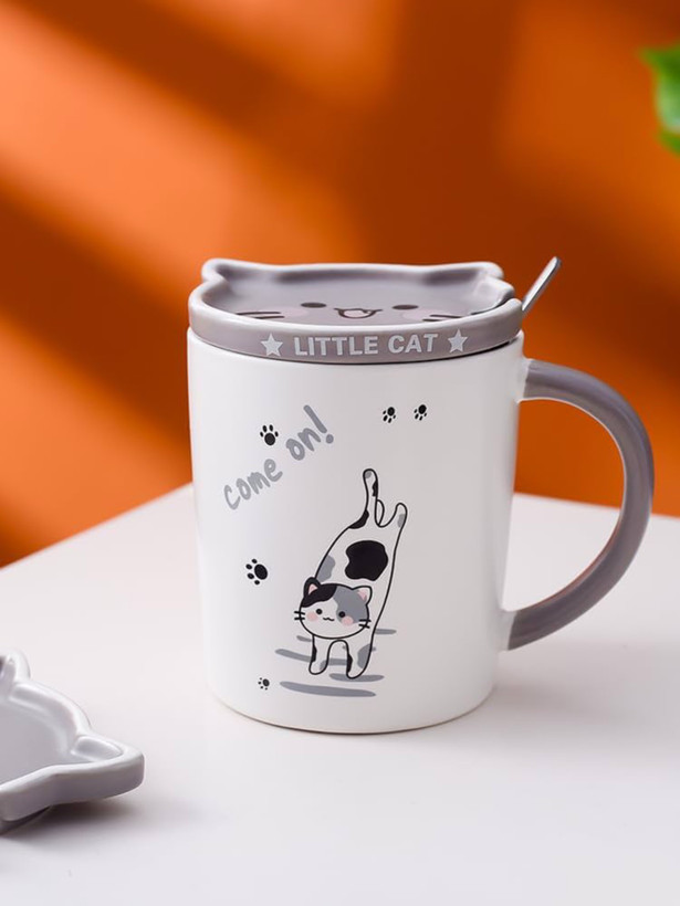 عکس صنعتی ماگ گربه نعلبکی دار به همراه قاشق روی زیر لیوانی چوبی روی میز سفید با پشت زمینه ی نارنجی از نمای رو به رو