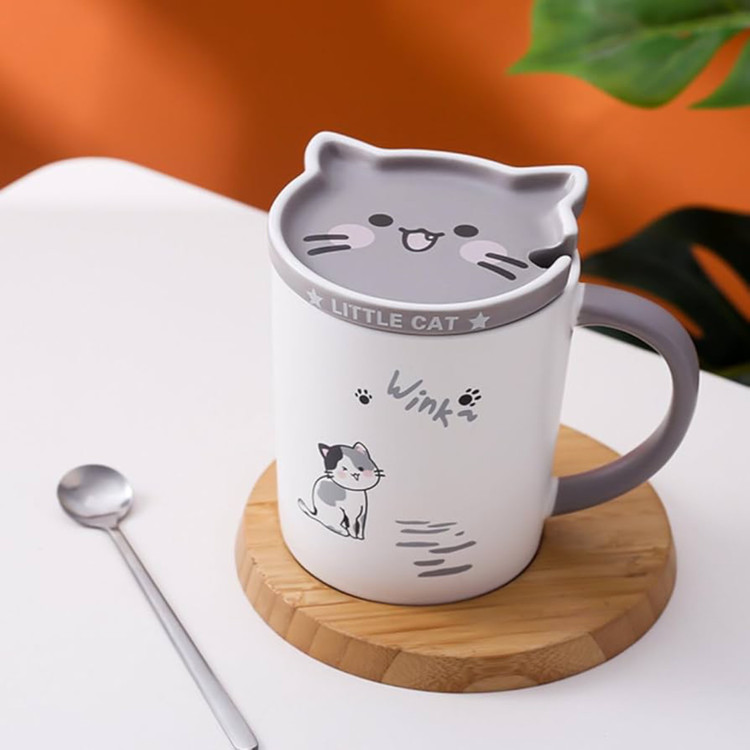 عکس صنعتی ماگ گربه نعلبکی دار به همراه قاشق روی زیر لیوانی چوبی روی میز سفید با پشت زمینه ی نارنجی