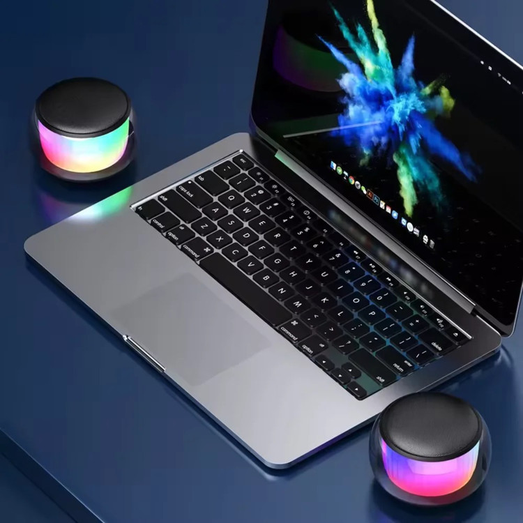 دو عدد اسپیکر LED دار مدل SW102 کنار لپتاپ روی میز سرمه ای از نمای بالا