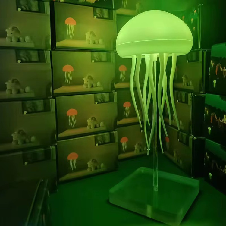 چراغ خواب عروس دریایی معلق روی پایه در حال نمایش نور فسفری رنگ و تعداد زیادی از جعبه ی این محصول در پشت زمینه