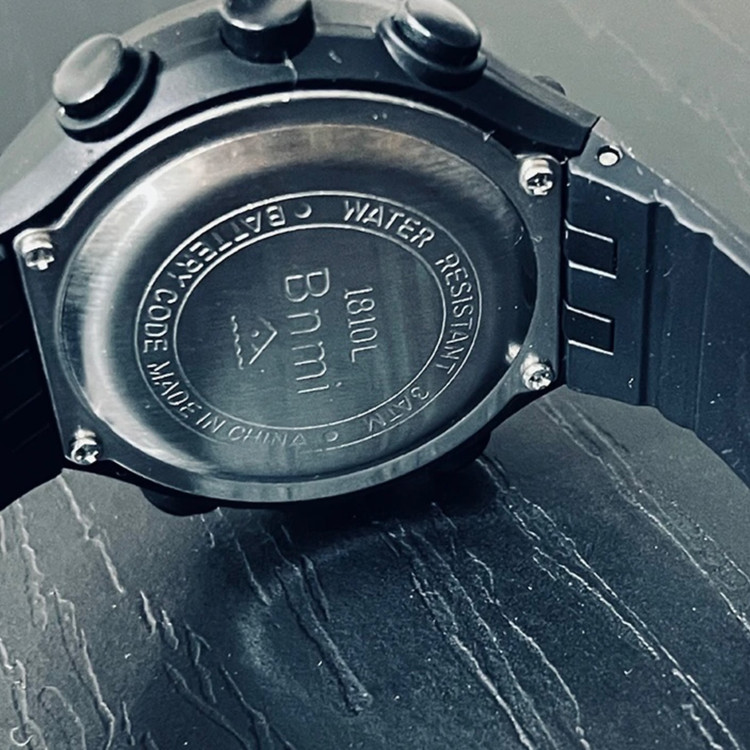 نمای پشت و نمایش مارک و مدل ساعت و جایگاه استیل باطری ساعت ضد آب بنمی رنگ مشکی روی میز چوبی مشکی